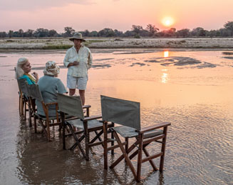 Bilimungwe manager Alex Steward has a surprise for her guests: a sundowner, barefoot in the Luangwa River,  with the Chindeni Hills on the horizon.   